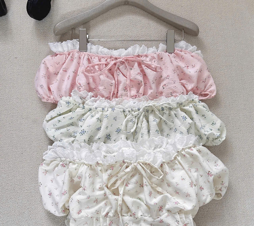 Three pairs of ruffled bloomers in pink, cream, and white floral prints, hanging on a wooden hanger against a neutral beige background.