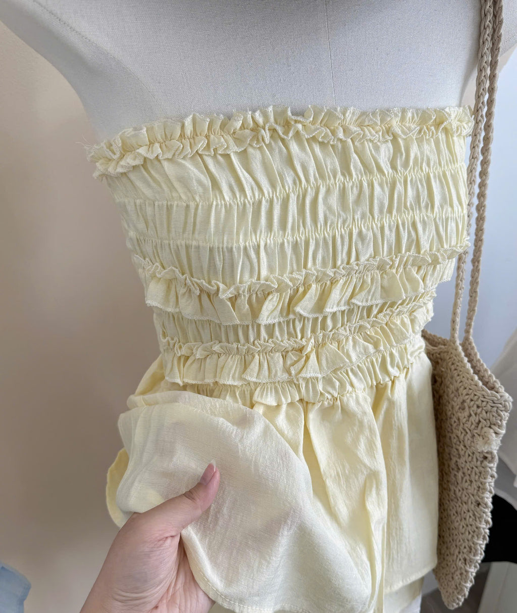 A yellow-colored smocked ruffle top displayed on a mannequin, with a hand holding up the gathered fabric to show its texture and drape.