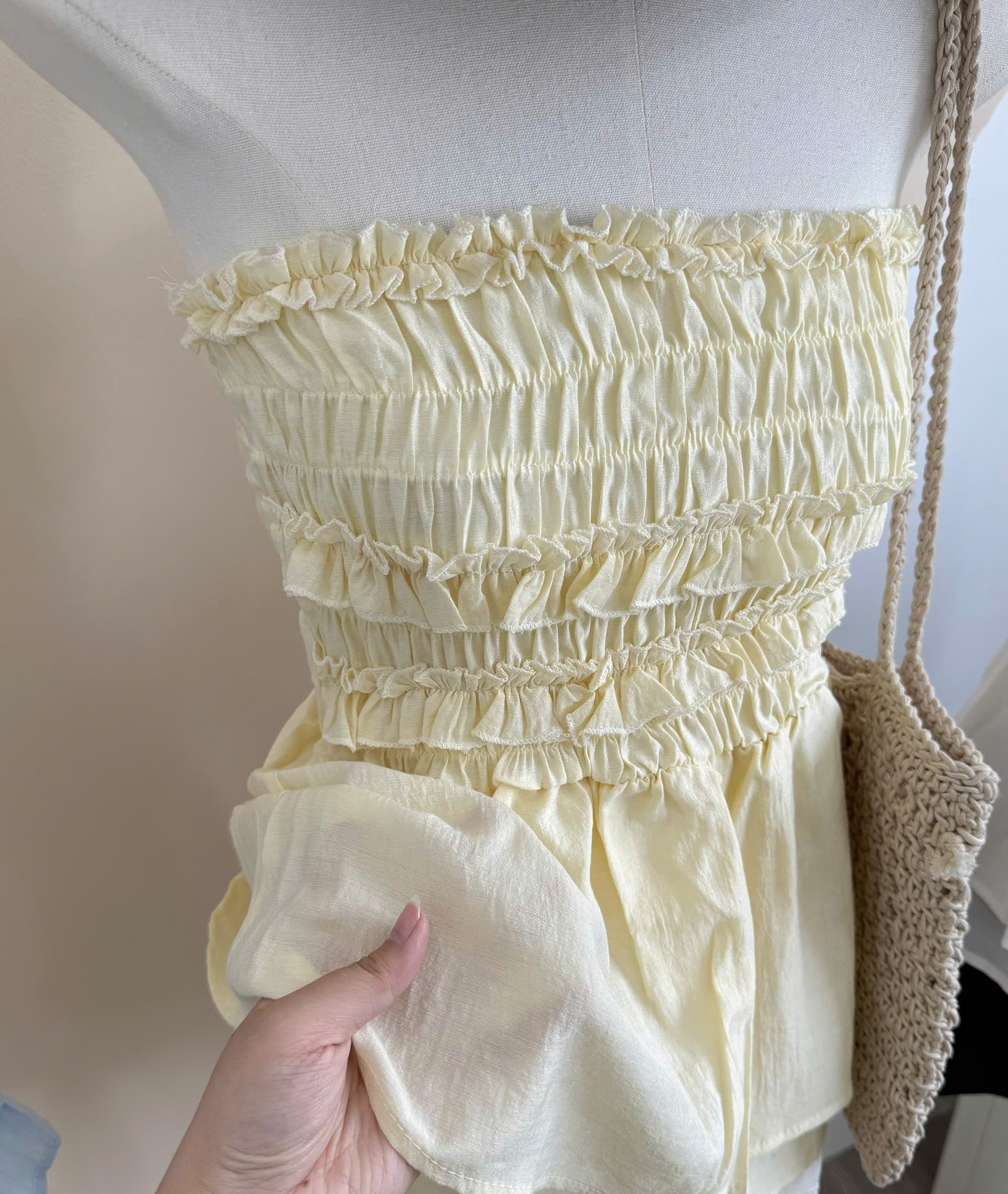 A yellow-colored smocked ruffle top displayed on a mannequin, with a hand holding up the gathered fabric to show its texture and drape.