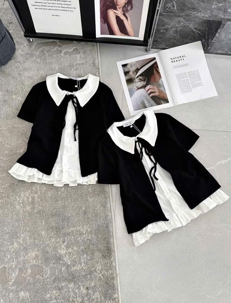 Two black short-sleeve tops with white Peter Pan collars and white ruffled underskirts, arranged on a gray tiled floor with magazine pages in the background.