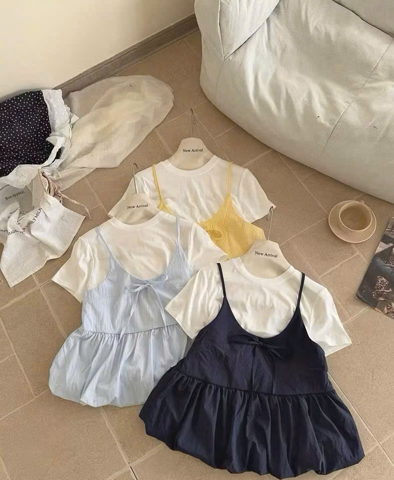 Three short-sleeve dress outfits laid out on a beige tiled floor: a light blue version, a pale yellow version, and a dark navy version, each styled over a white short-sleeve top. No people or animals are present.