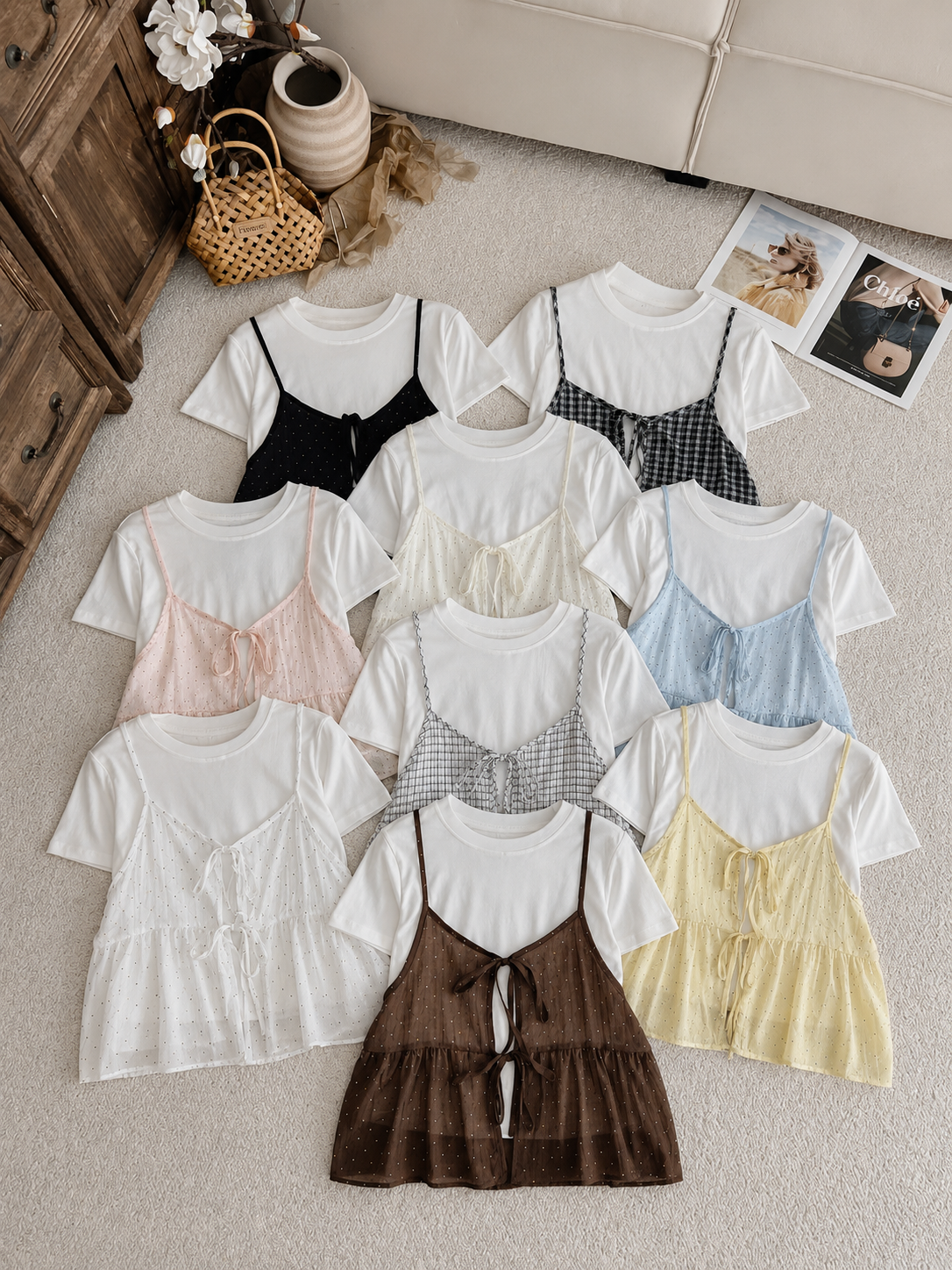 A flat-lay display of ten different color variations of a short-sleeve white t-shirt with a matching crinkled camisole vest, arranged on a beige carpet with decorative props.