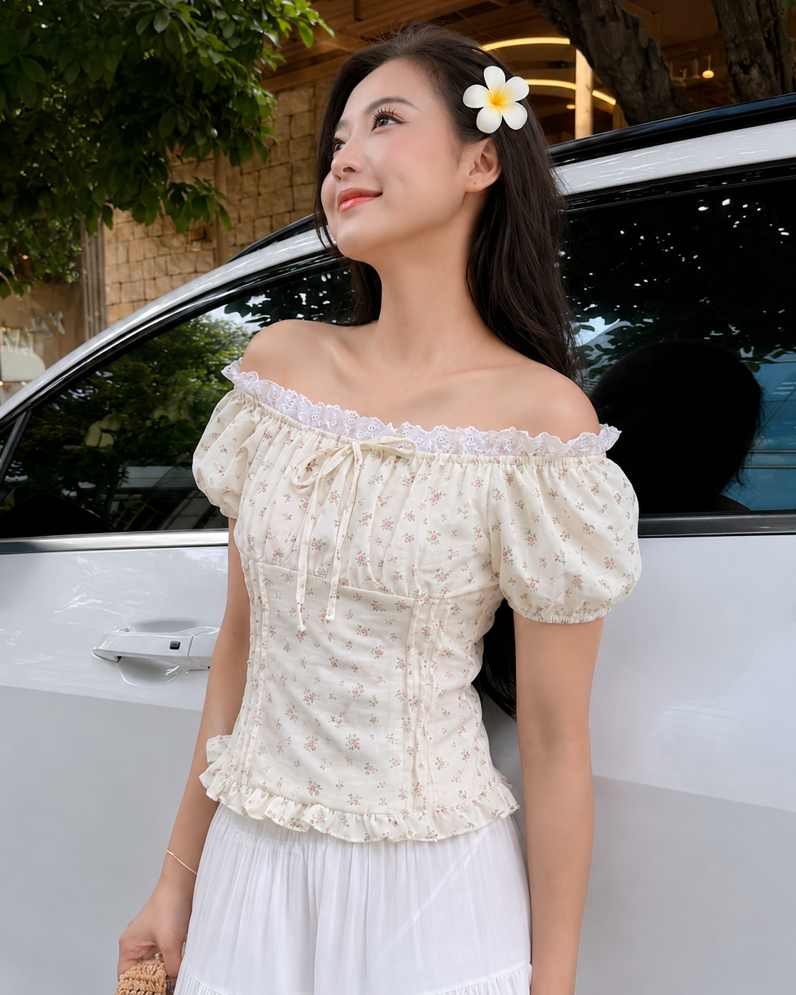 A woman wearing a cream off-the-shoulder puff-sleeve top with a tiny floral print and white ruffled trim, paired with a white skirt, standing next to a white car outdoors.