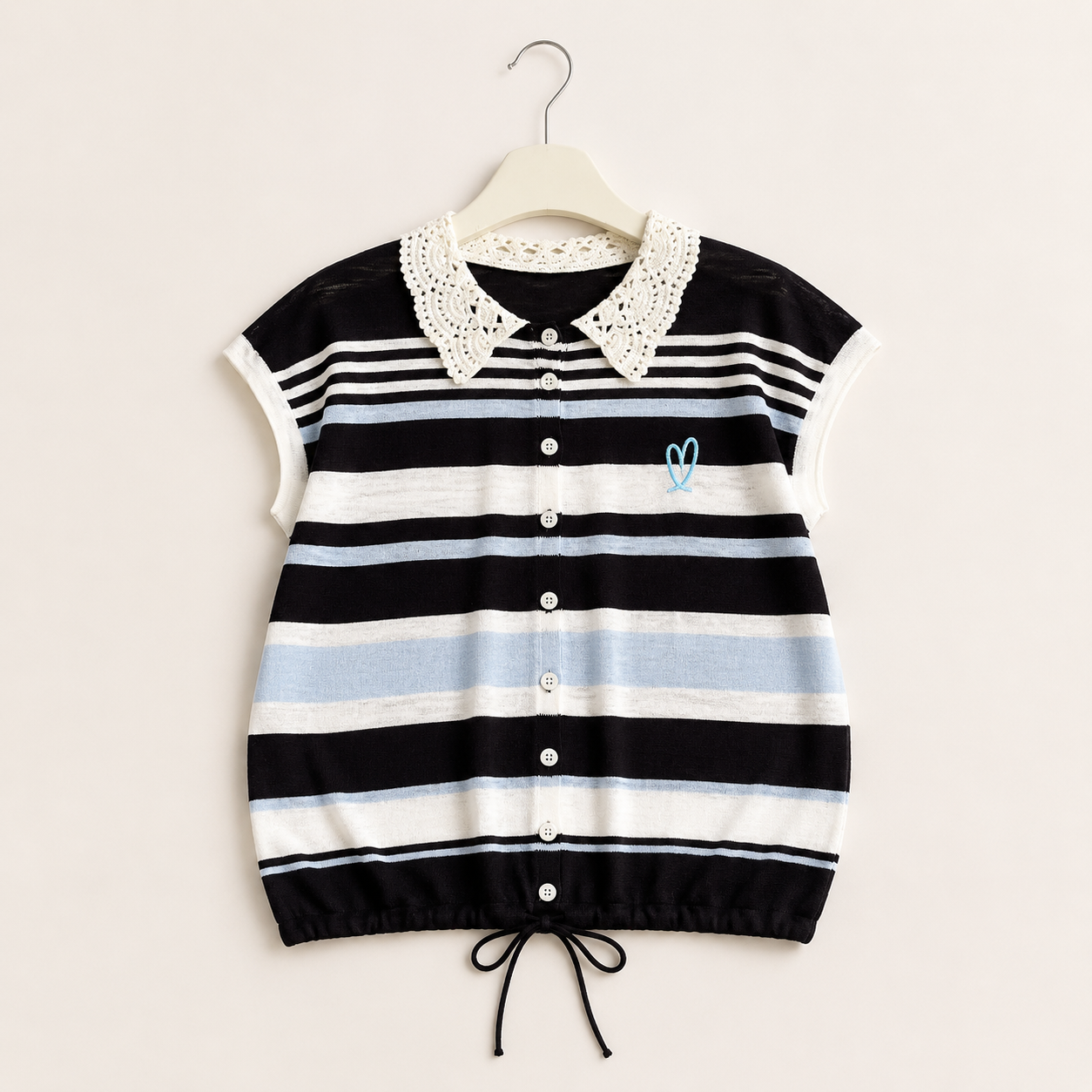A short-sleeve knit top, featuring horizontal stripes in black, white, and light blue, with a white crochet collar and a small light blue embroidered heart on the chest. It is shown hanging on a wooden hanger against a light beige background.
