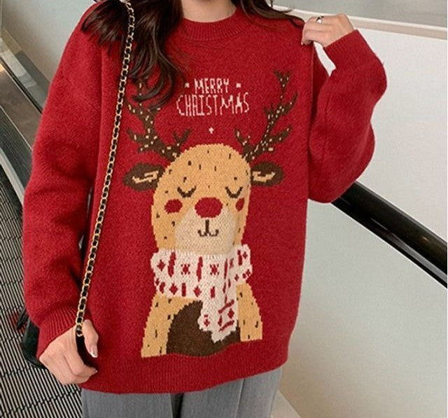 A person wearing a red knit sweater with a large cartoon reindeer graphic and the words “MERRY CHRISTMAS” across the chest, photographed indoors near a staircase.