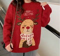 A person wearing a red knit sweater with a large cartoon reindeer graphic and the words “MERRY CHRISTMAS” across the chest, photographed indoors near a staircase.